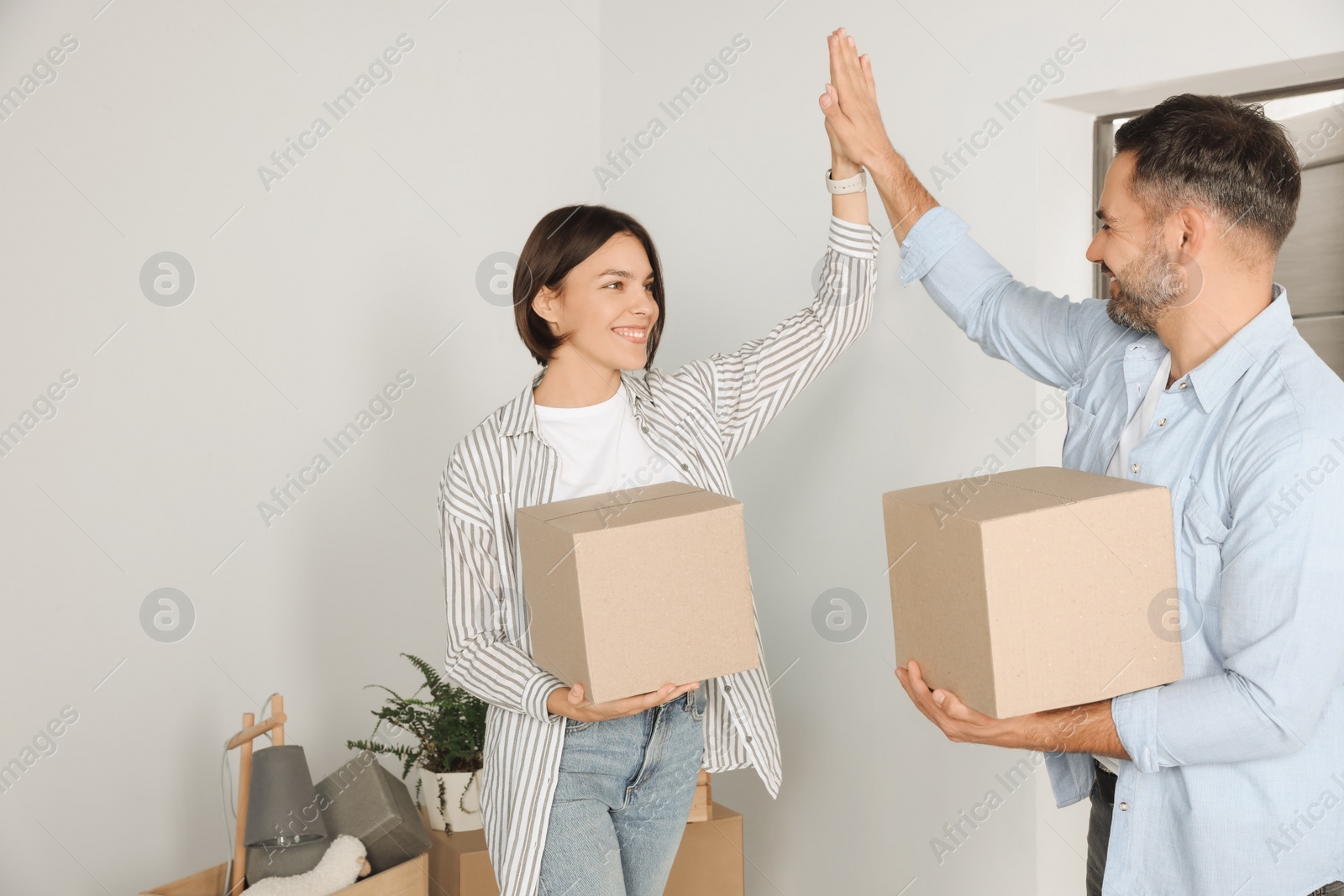 Photo of Happy couple with moving boxes giving high five in new apartment