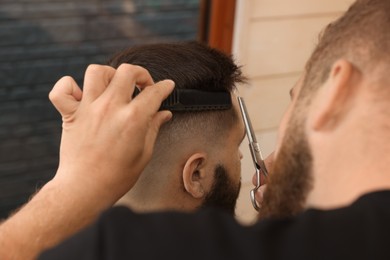 Photo of Professional hairdresser working with client in barbershop, closeup