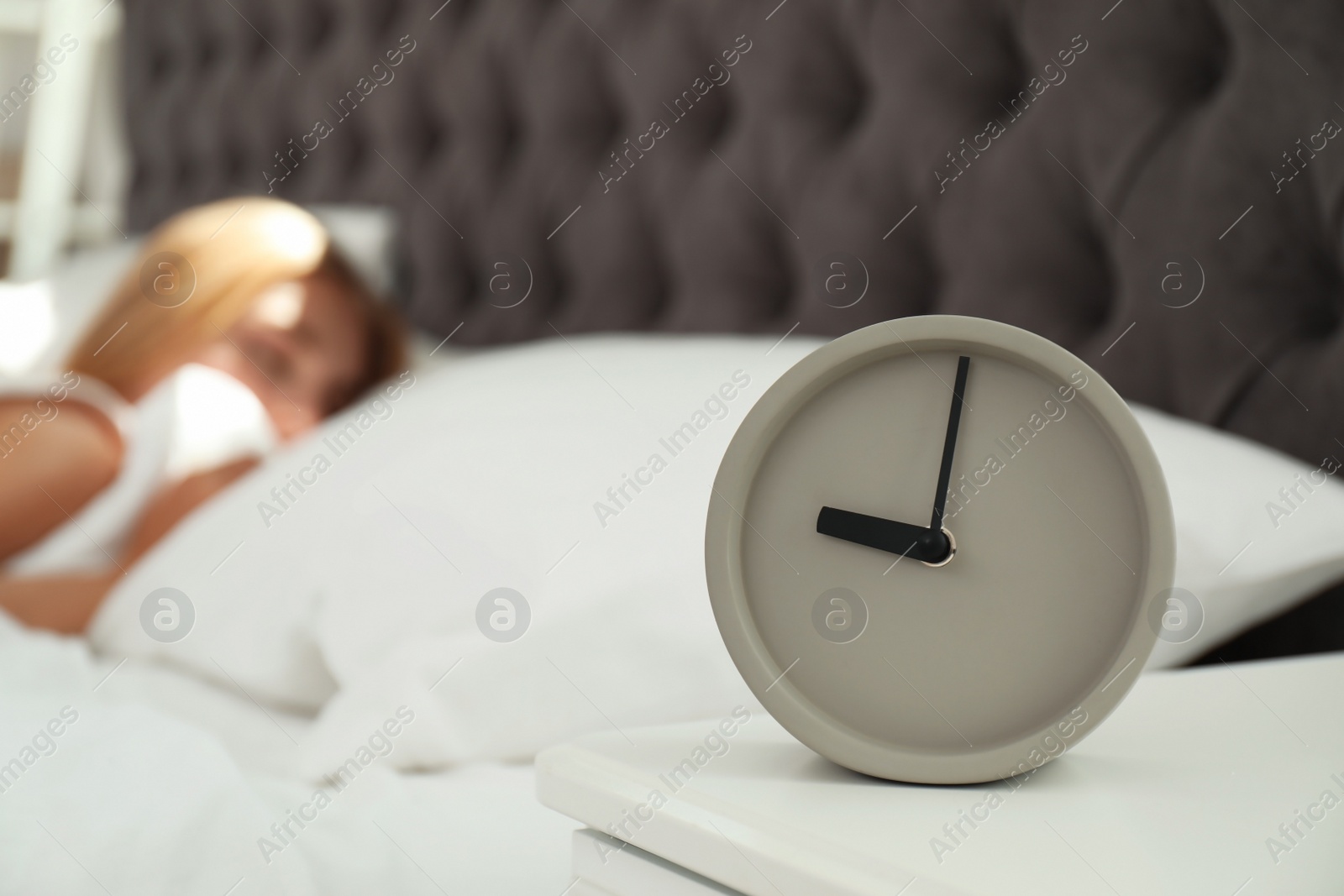 Photo of Analog alarm clock and blurred sleepy woman on background. Time of day