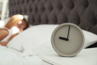 Analog alarm clock and blurred sleepy woman on background. Time of day