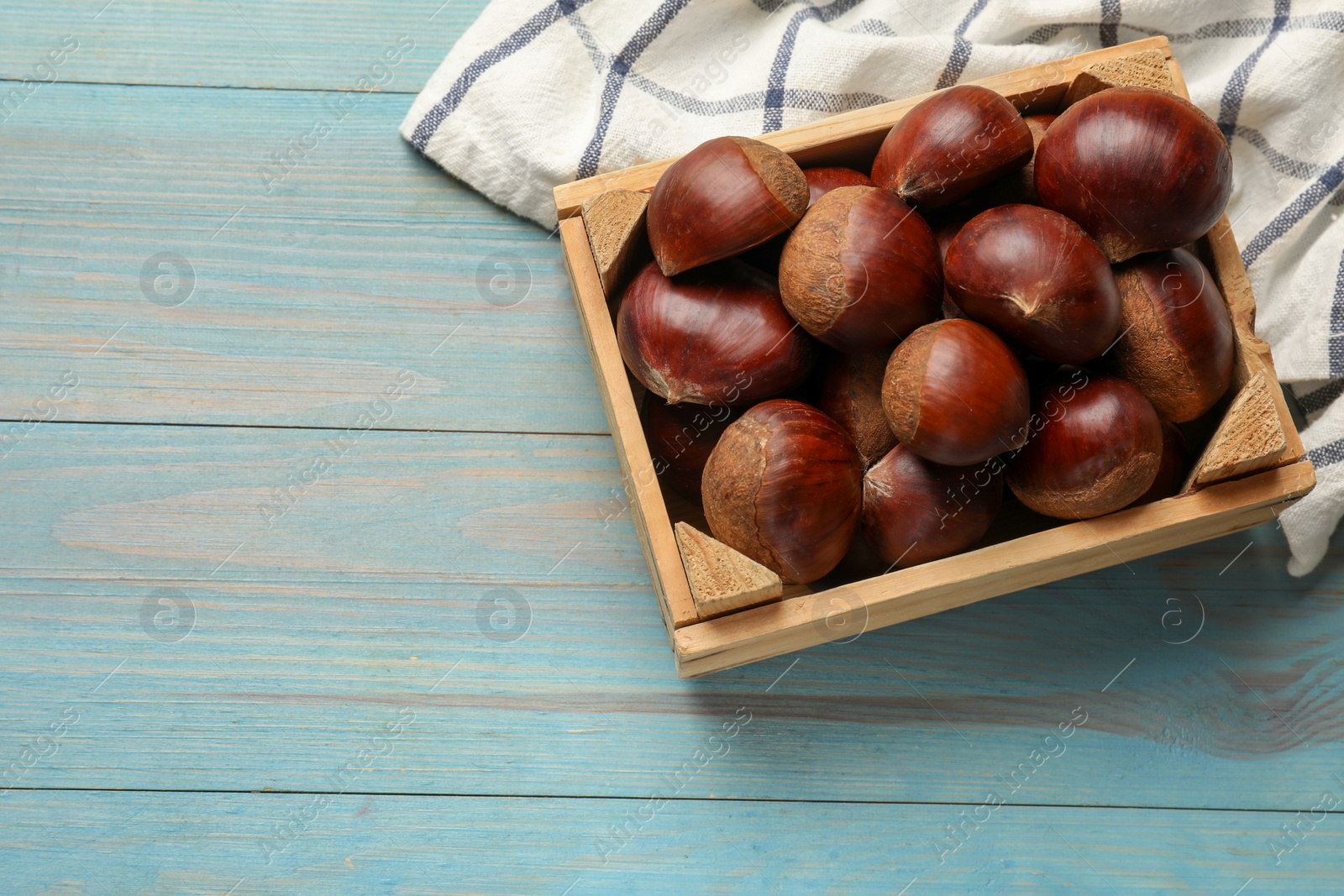 Photo of Roasted edible sweet chestnuts in crate on light blue wooden table, top view. Space for text