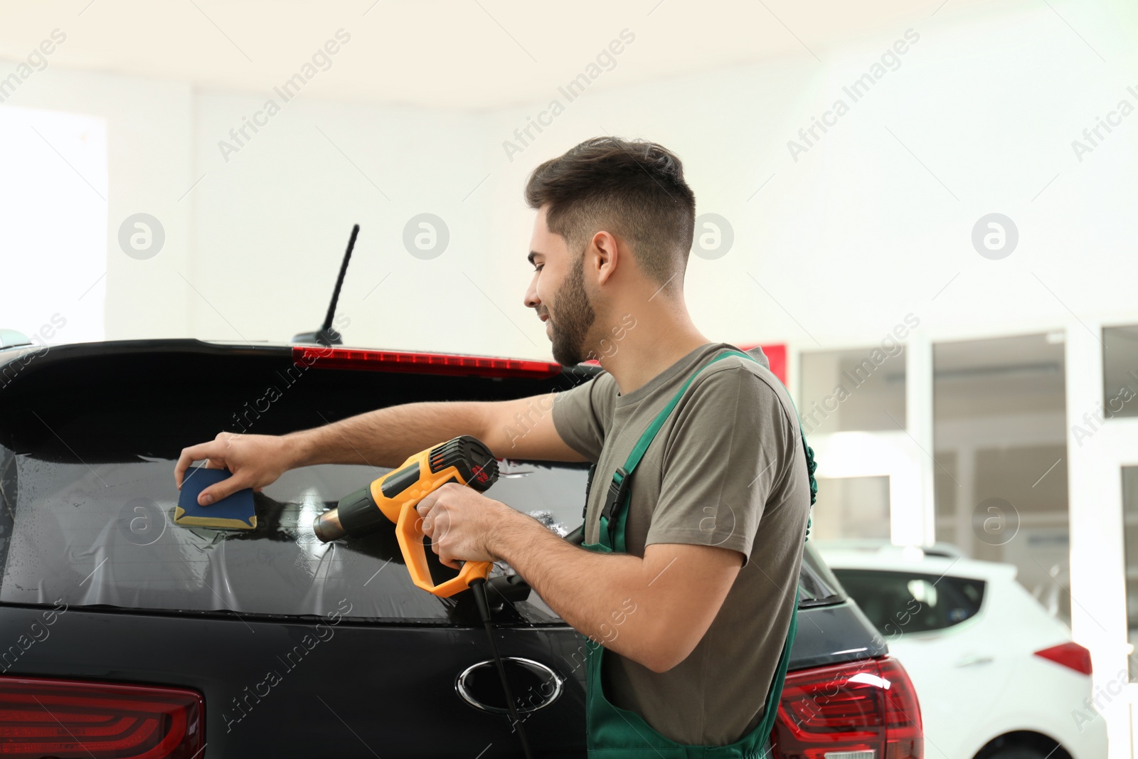 Photo of Worker tinting car window with heat gun in workshop