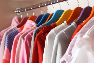 Photo of Stylish girl's clothes hanging in wardrobe, closeup