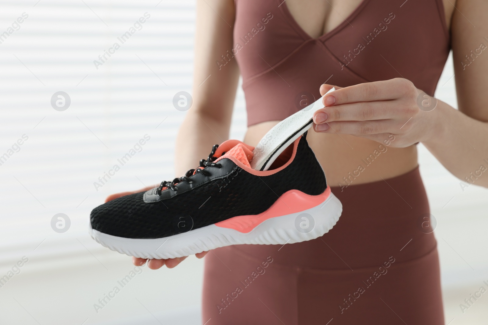 Photo of Sporty woman putting orthopedic insole into shoe indoors, closeup. Foot care