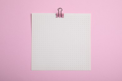 Sheet of paper with clip on pink background, top view