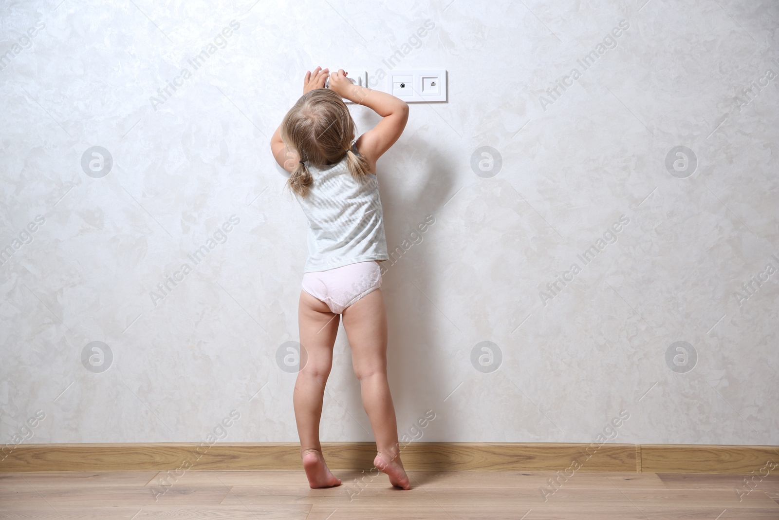 Photo of Little child playing with electrical socket indoors, back view. Dangerous situation