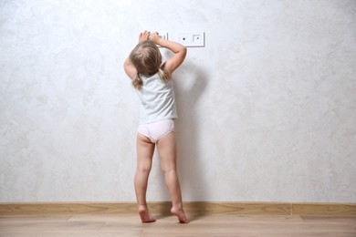 Little child playing with electrical socket indoors, back view. Dangerous situation