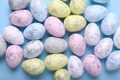 Many painted Easter eggs on light blue background, flat lay.