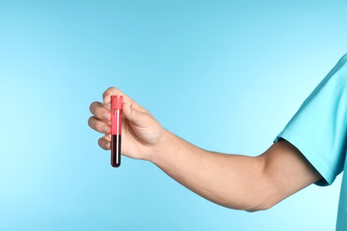 Male doctor holding test tube with blood sample on color background, closeup. Medical object