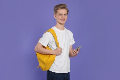Photo of Teenage boy with backpack using smartphone on purple background