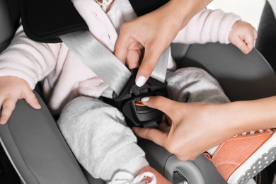 Mother fastening baby to child safety seat inside car