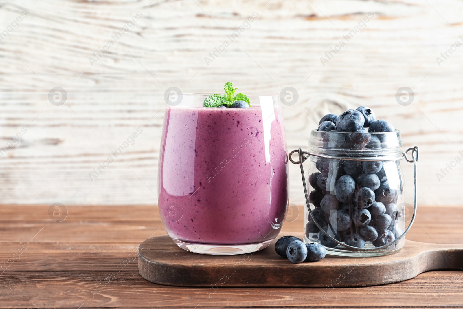 Photo of Glass of smoothie and jar with blueberries on wooden table