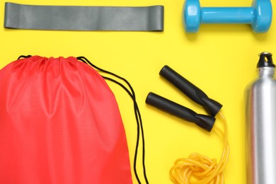 Photo of Red drawstring bag and sports equipment on yellow background, flat lay