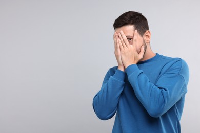 Photo of Embarrassed man covering face on light grey background. Space for text