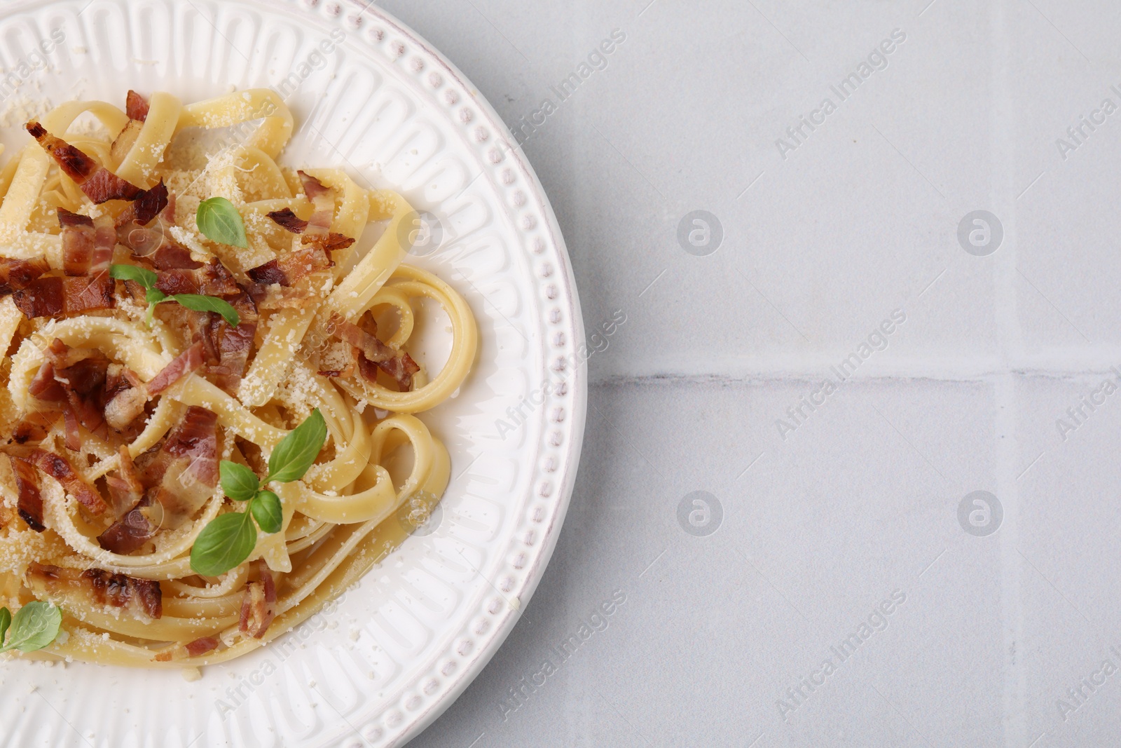 Photo of Tasty pasta with bacon and basil on white tiled table, top view. Space for text