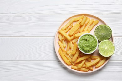 Plate with french fries, lime and avocado dip on white wooden table, top view. Space for text