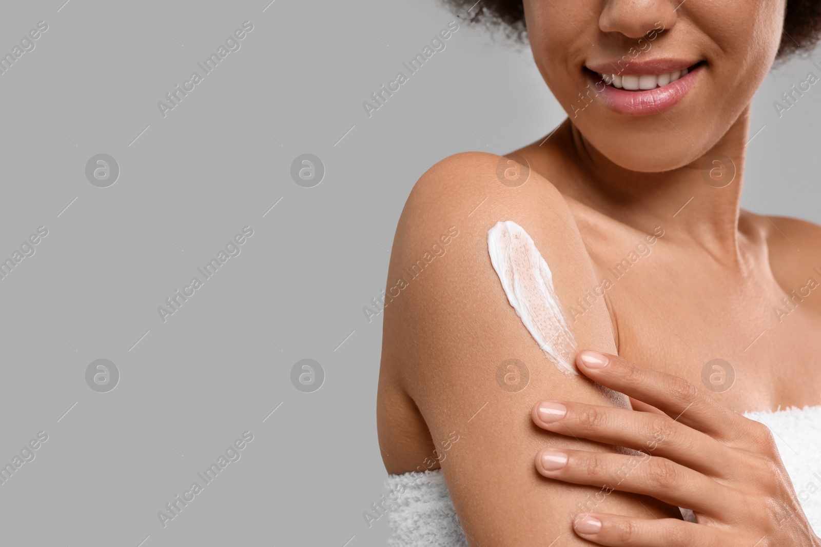 Photo of Young woman applying body cream onto arm on grey background, closeup. Space for text