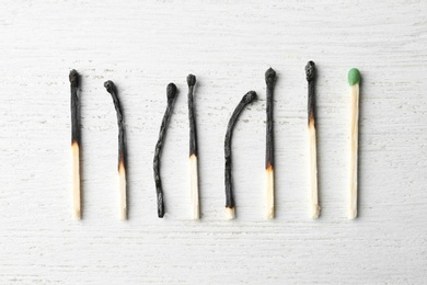 Photo of Row of burnt matches and whole one on wooden background, flat lay. Uniqueness concept
