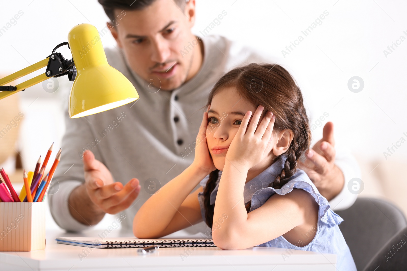 Photo of Father scolding his daughter while helping with homework at table indoors