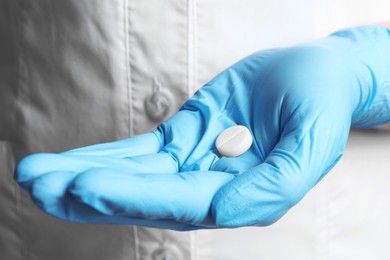 Photo of Doctor in medical glove holding pill, closeup view