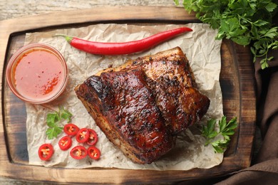 Photo of Piece of baked pork belly served with sauce and chili pepper on wooden table, top view