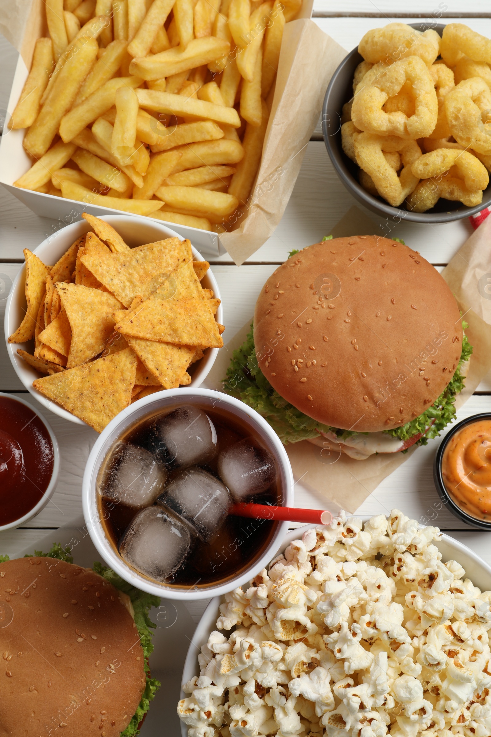 Photo of Burgers, chips and other fast food on white wooden table, flat lay