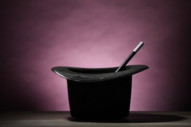 Photo of Magician's hat and wand on wooden table against dark background