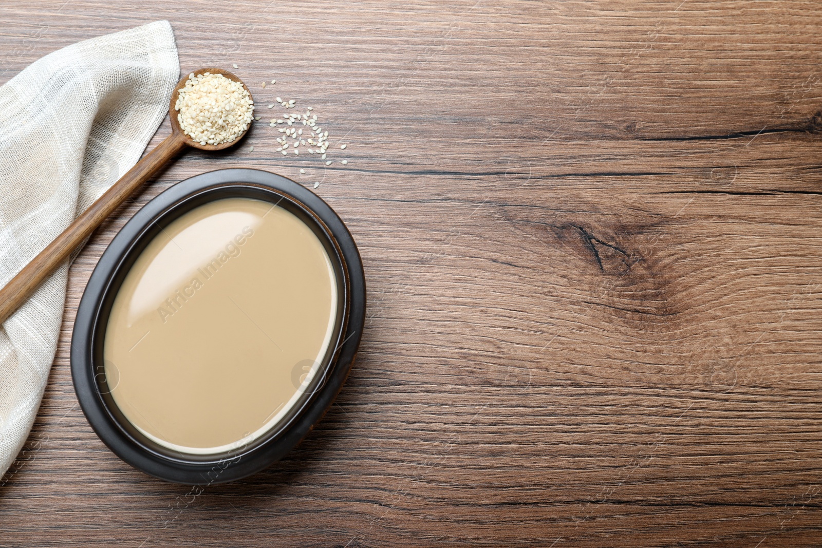 Photo of Tasty sesame paste, seeds and spoon on wooden table, flat lay. Space for text