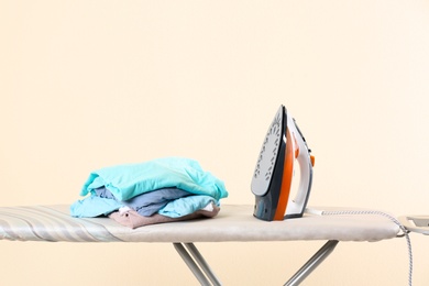 Photo of Board with modern iron and clean laundry on beige background