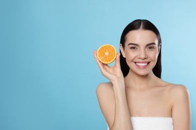 Woman holding half of orange on light blue background, space for text. Spa treatment