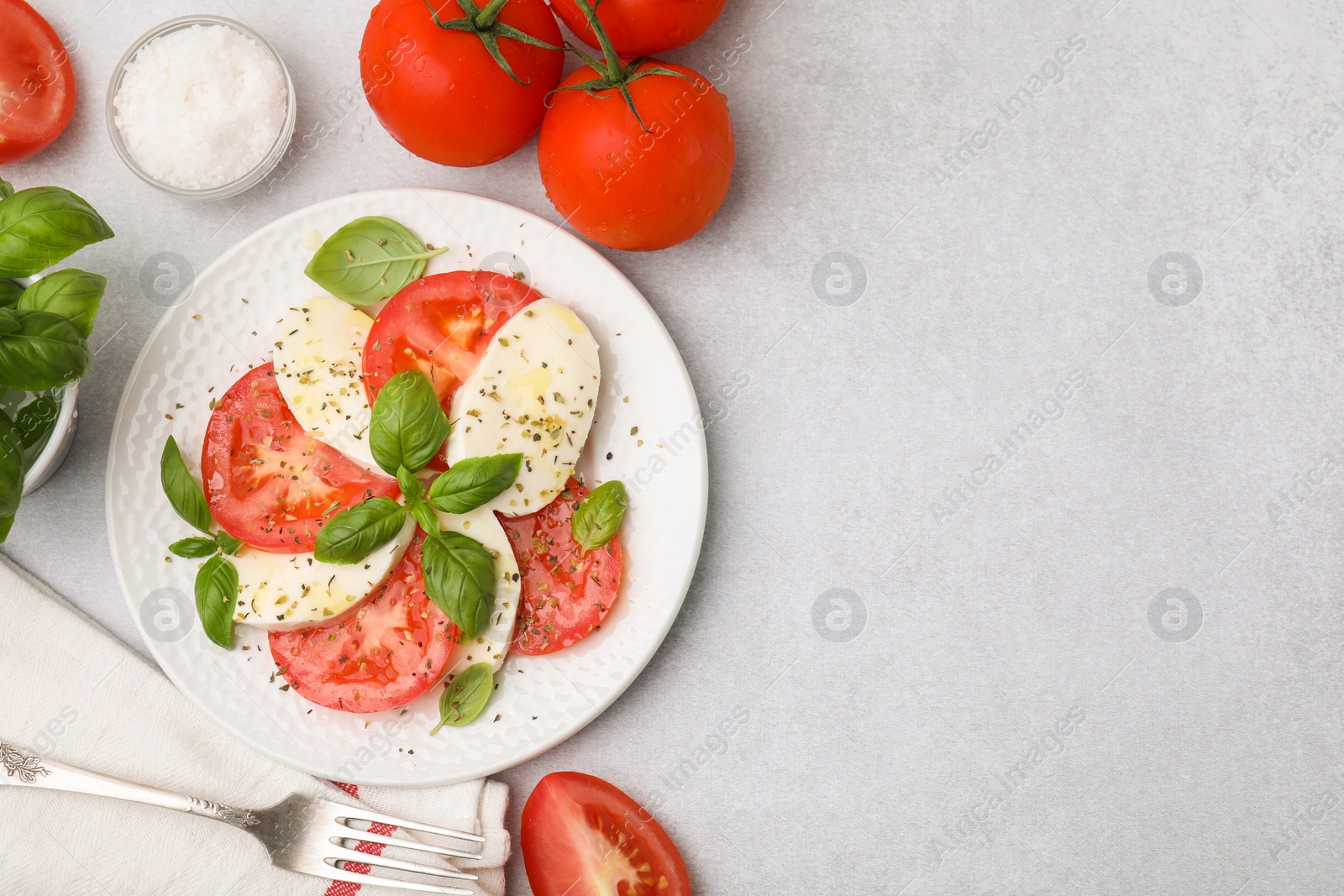 Photo of Plate of delicious Caprese salad with herbs and ingredients on light grey table, flat lay. Space for text