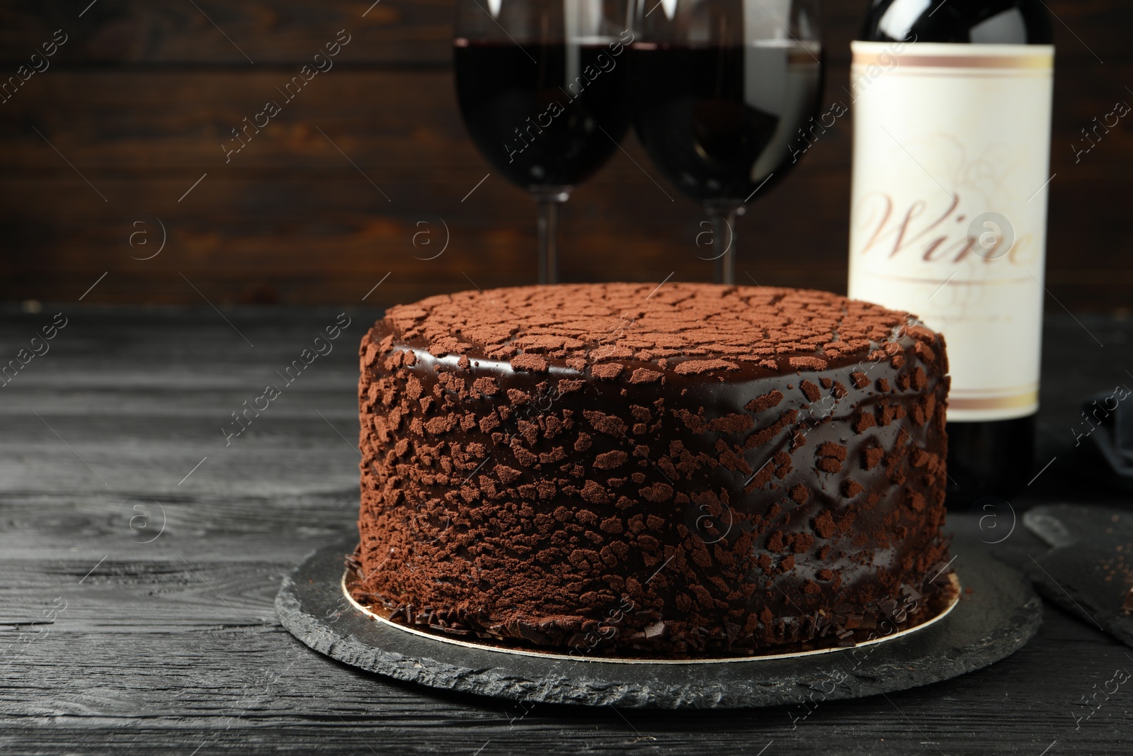 Photo of Delicious chocolate truffle cake and red wine on black wooden table