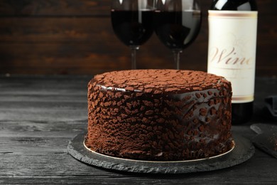 Photo of Delicious chocolate truffle cake and red wine on black wooden table