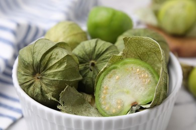 Fresh green tomatillos with husk in bowl on table, closeup
