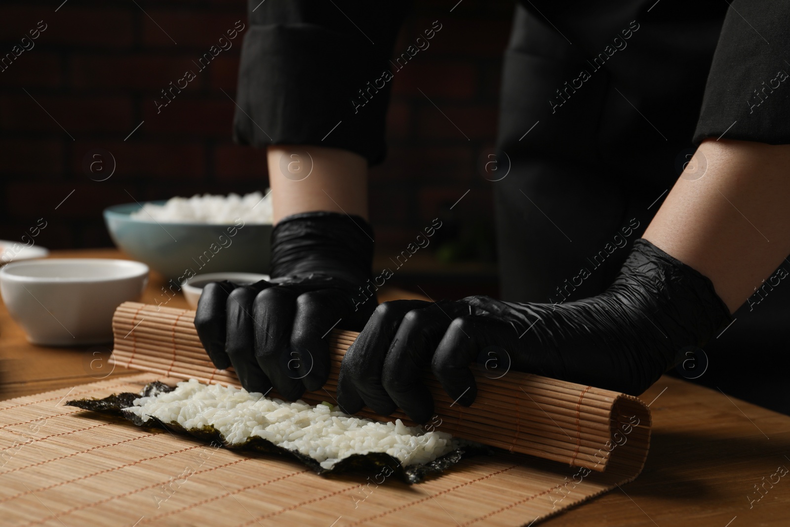 Photo of Chef in gloves making sushi roll at wooden table, closeup