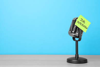 Photo of Retro microphone and reminder note with words JOB INTERVIEW on wooden table against light blue background, space for text
