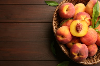 Photo of Fresh sweet peaches in wicker basket on wooden table, top view. Space for text