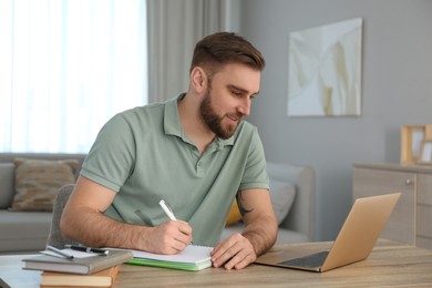 Photo of Young man taking notes during online webinar at table indoors