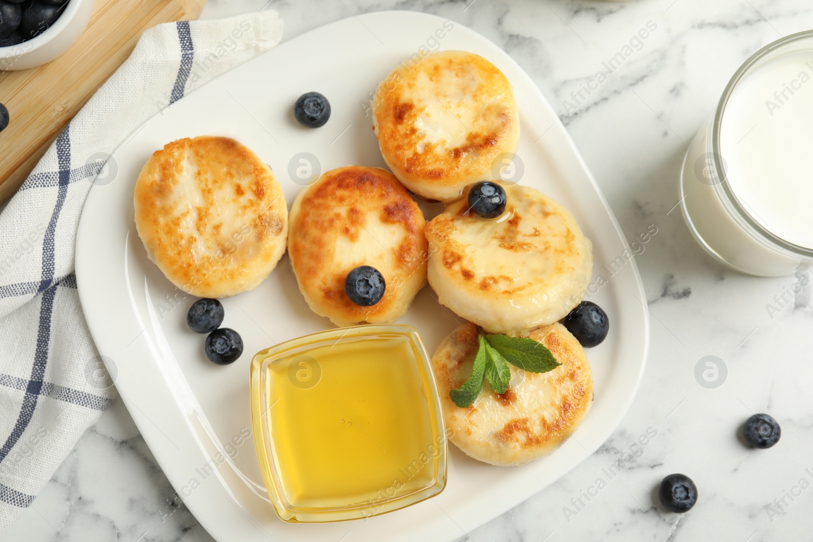 Photo of Delicious cottage cheese pancakes with blueberries and honey on white marble table, flat lay