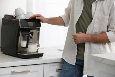 Photo of Young man preparing fresh aromatic coffee with modern machine in kitchen, closeup