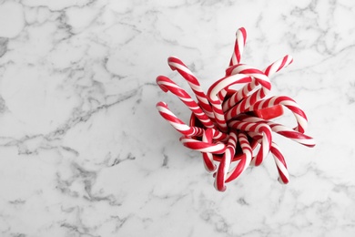 Photo of Candy canes in cup on white marble background, top view with space for text. Traditional Christmas treat