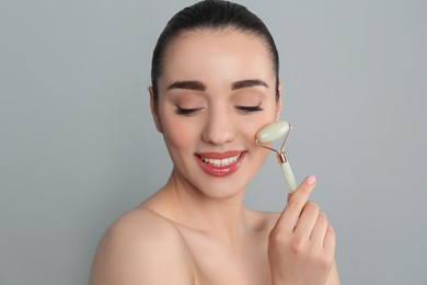 Photo of Woman using natural jade face roller on grey background