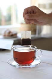 Photo of Woman taking tea bag out of cup at white wooden table indoors, closeup