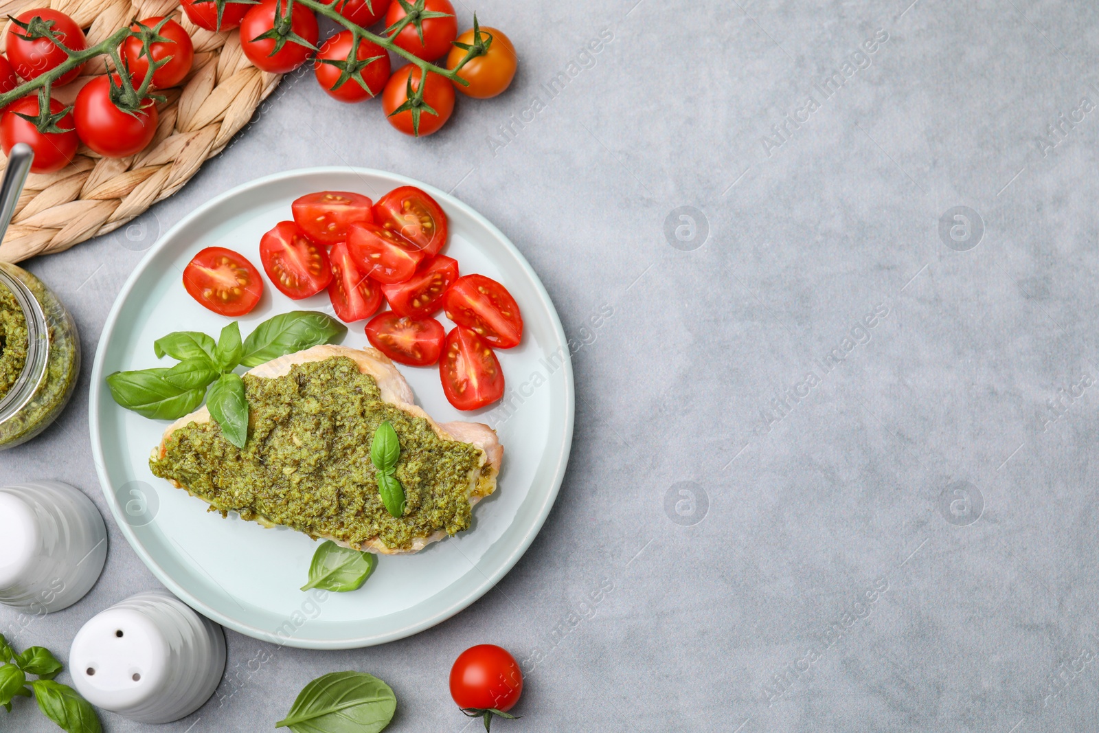 Photo of Delicious chicken breast with pesto sauce and tomatoes on light gray table, flat lay. Space for text