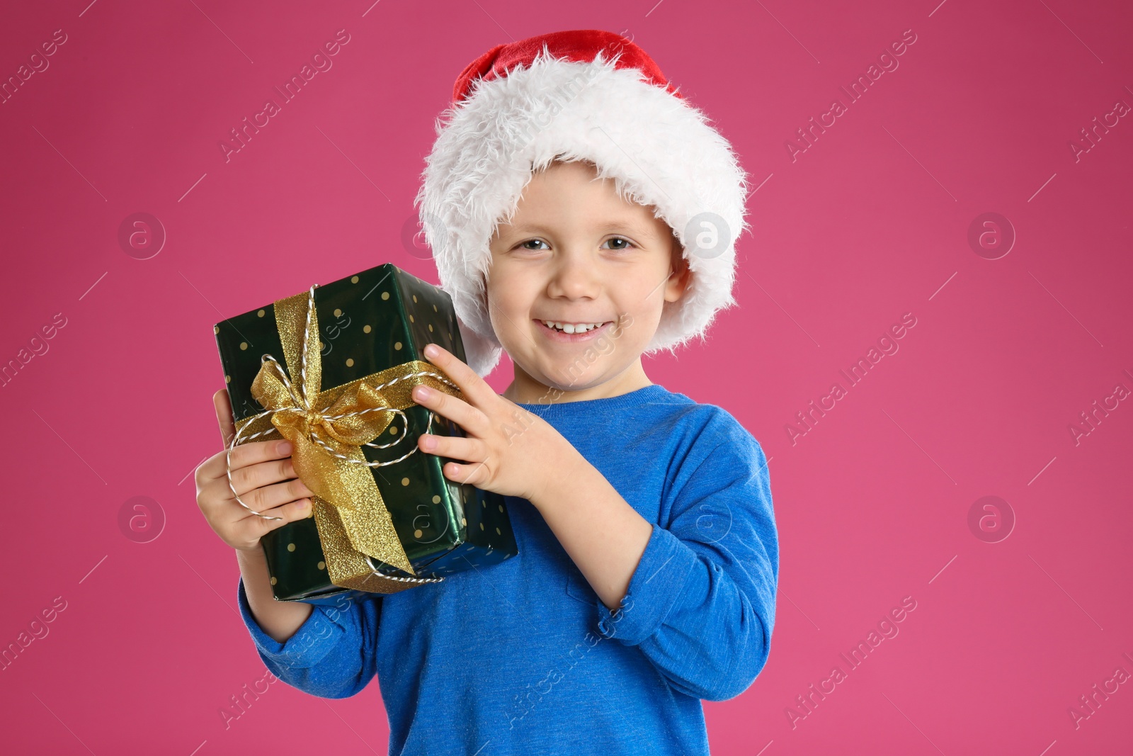 Photo of Cute child in Santa hat with Christmas gift on pink background