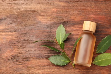 Photo of Bottle of bay essential oil and fresh leaves on wooden table, flat lay. Space for text