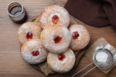 Photo of Delicious donuts with jelly and powdered sugar on wooden table, flat lay
