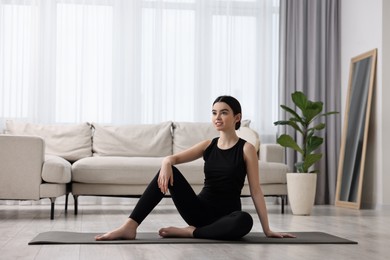 Beautiful girl sitting on yoga mat at home