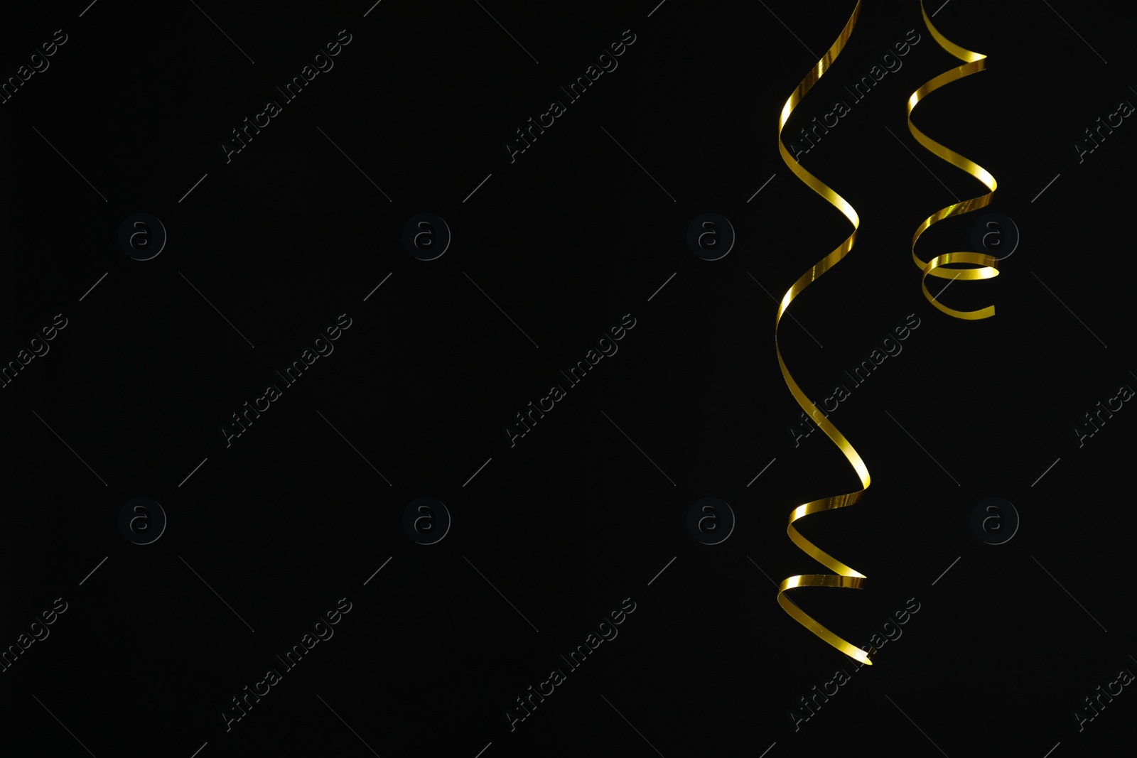 Photo of Shiny golden serpentine streamers on black background. Space for text