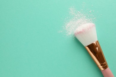 Photo of Makeup brush with rice loose face powder on turquoise background, top view. Space for text